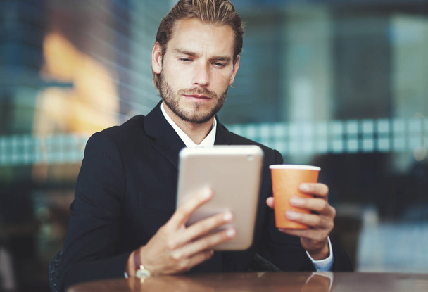 Handsome businessman enjoying a cup of coffee and looking his tablet - Foto, afbeelding