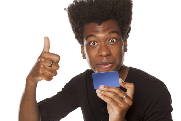 Hymyilevä ja positiivinen onnellinen nuori afroamerikkalainen kaveri, jolla on luottokortti ja joka näyttää peukaloa valkoisella taustalla
 - Valokuva, kuva