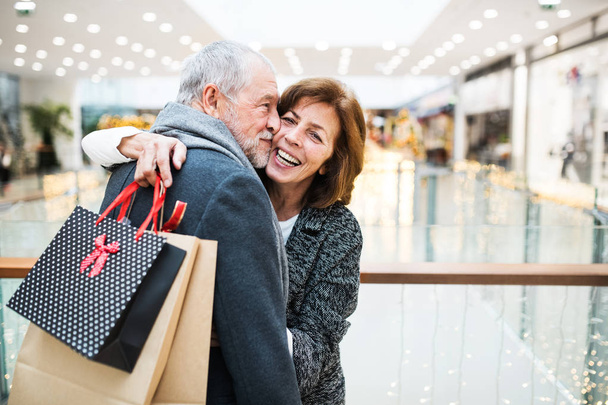 Happy senior couple with paper bags in shopping center, hugging. - Fotografie, Obrázek