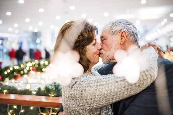 A happy senior couple standing in shopping center, kissing. - 写真・画像