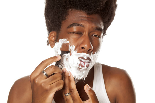 Молодой красивый афроамериканец сбривает бороду на белом фоне.
 - Фото, изображение