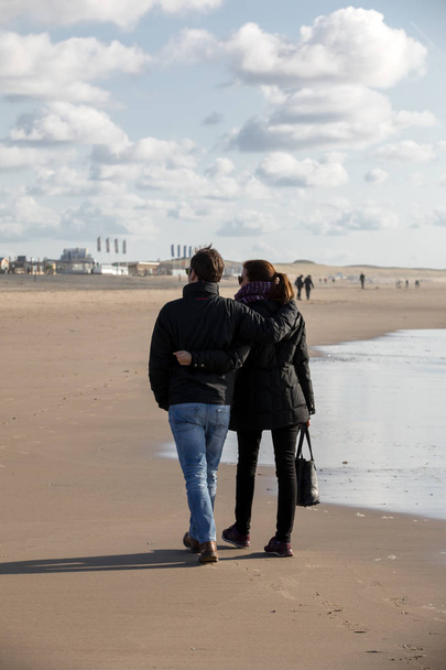 Katwijk, Netherlands - April 23, 2017: A woman and a man are walking on a sunny day along the beach in Katwijk. Netherlands - Φωτογραφία, εικόνα