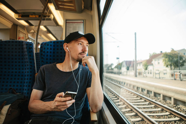 Genç bir adam bir müzik veya podcast bir tren seyahat ederken dinler - Fotoğraf, Görsel