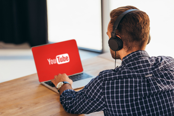 partial view of man in headphones using laptop with youtube logo on screen in office - Photo, Image