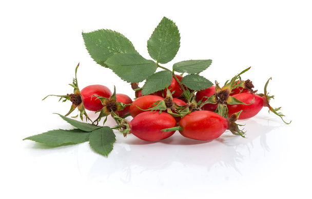 Fresh red rose hips with leaves on a white reflective surface - Photo, Image
