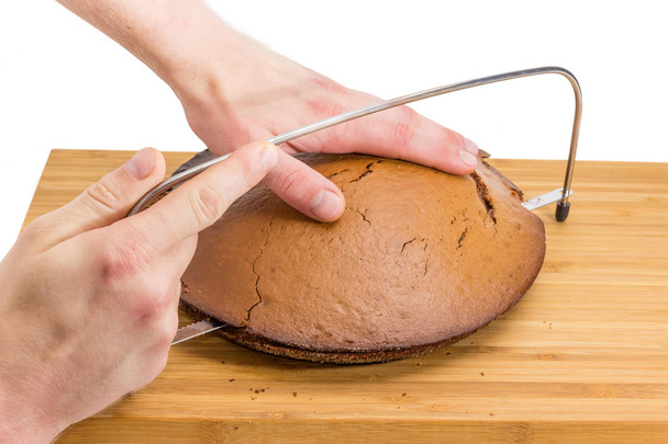 Резак для выравнивания тортов с зазубренным ножом и регулировка высоты слоя в человеческих руках во время разрезания пустого торта на деревянной бамбуковой режущей доске на белом фоне
 - Фото, изображение
