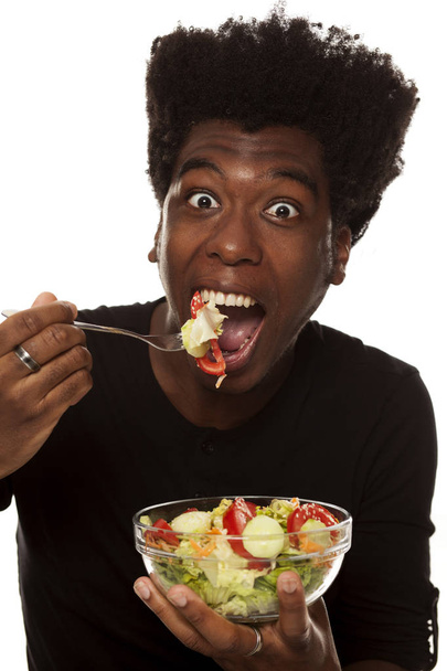 Joven chico afroamericano guapo comiendo ensalada aislado sobre un fondo blanco. concepto de alimentos saludables
 - Foto, imagen