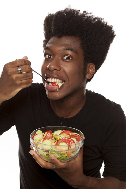 Joven chico afroamericano guapo comiendo ensalada aislado sobre un fondo blanco. concepto de alimentos saludables
 - Foto, Imagen