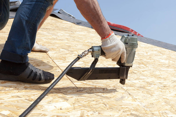 Trabajador constructor de techos con pistola de clavos instalando Oriented Strand Board o panel OSB en una casa nueva en construcción
 - Foto, Imagen