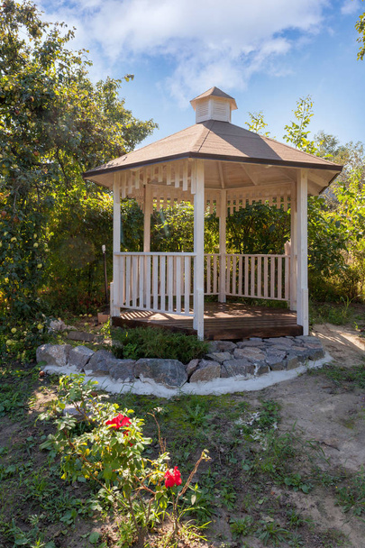 schön gestalteter weißer Gartenpavillon oder Pavillon im Hinterhof mit Rosen im Vordergrund - Foto, Bild