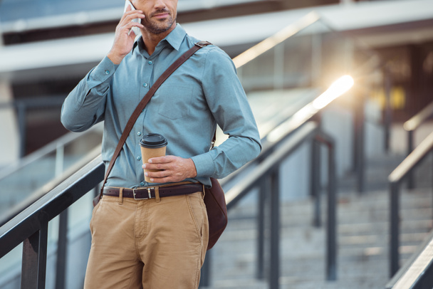 bijgesneden schot van zakenman holding koffie te gaan en praten door de smartphone op trappen - Foto, afbeelding