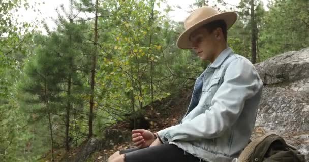 Junger Mann sitzt auf Klippe im Wald - Filmmaterial, Video