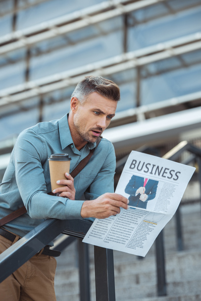 zszokowany mężczyzna trzyma kawę na wynos i czytanie gazety biznes  - Zdjęcie, obraz