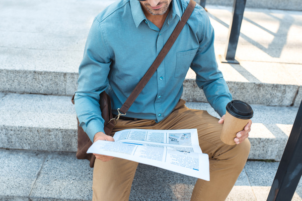 plan recadré d'homme d'affaires avec du café pour aller s'asseoir sur les escaliers et lire le journal
 - Photo, image