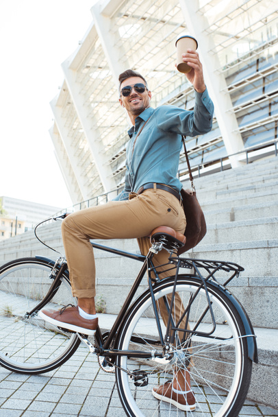 自転車の上に座って、使い捨てのコーヒー カップを保持している笑みを浮かべて男の低角度のビュー - 写真・画像
