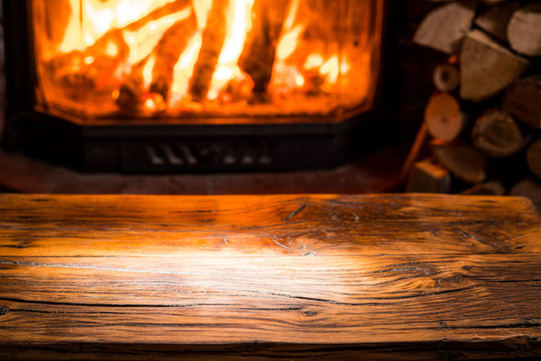 Vieille table en bois et cheminée avec feu chaud à l'arrière-plan. - Photo, image