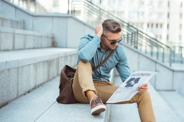 stylish middle aged man sitting on stairs and reading business newspaper - Photo, Image