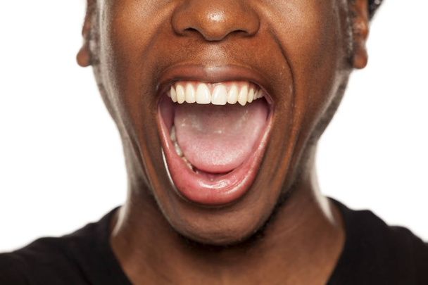 Vue rapprochée d'une bouche ouverte d'un jeune noir afro-américain sur fond blanc
 - Photo, image