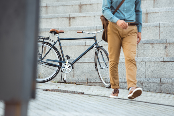 low section of stylish man walking on street, parked bicycle behind  - Foto, imagen