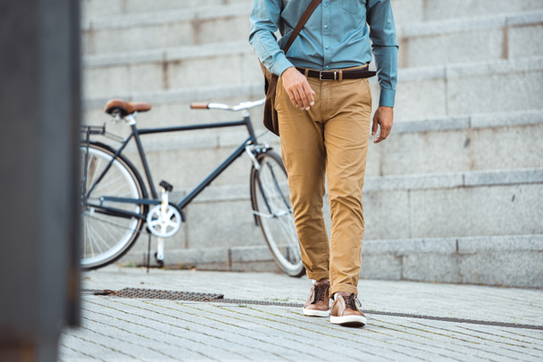 cropped shot of stylish man walking on street, parked bicycle behind  - Фото, изображение