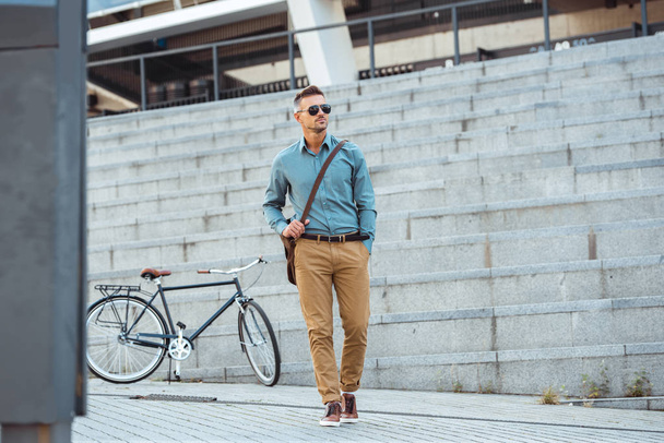handsome middle aged businessman in sunglasses walking on street, bicycle on background - Photo, Image