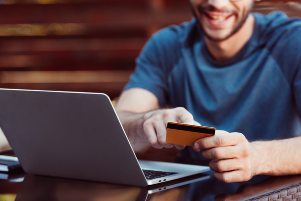 男のクレジット カードと通りのカフェのテーブルでノート パソコンでオンライン ショッピングのトリミングされた画像 - 写真・画像