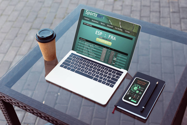 Laptop mit Sportwetten-Gerät, Smartphone und Kaffee im Pappbecher auf dem Tisch auf der Straße - Foto, Bild