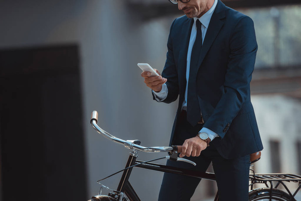 Schnappschuss von Geschäftsmann, der auf Fahrrad sitzt und Smartphone benutzt - Foto, Bild