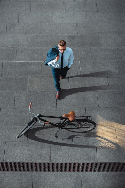 vista ad alto angolo di uomo d'affari che tiene giacca tuta e guardando la bicicletta sulla strada
   - Foto, immagini