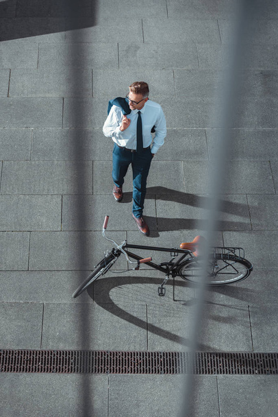 high angle view of businessman holding suit jacket and looking away near bike on street  - Fotó, kép