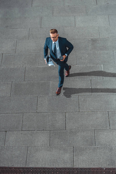 high angle view of businessman with paper cup and newspaper walking on street    - Photo, image