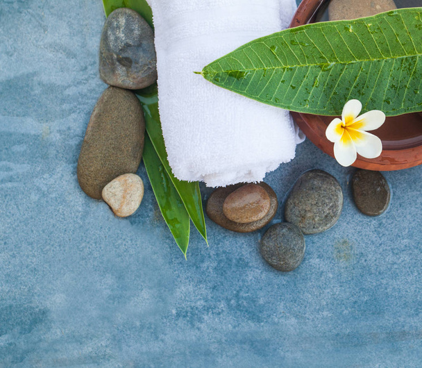 Bovenaanzicht van tropische witte bloem met stenen voor massagebehandeling op blauwe marmeren achtergrond. - Foto, afbeelding