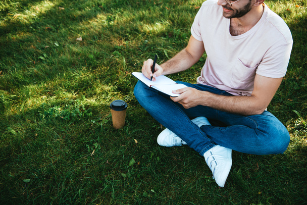 przycięty obraz człowieka, robiąc notatki na zielonej trawie w parku - Zdjęcie, obraz