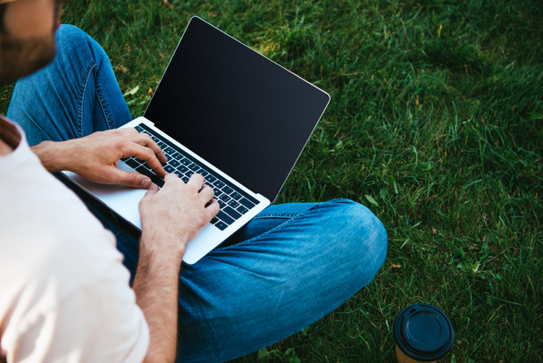 bijgesneden afbeelding van man met laptop met leeg scherm in park - Foto, afbeelding