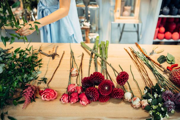 Tafel met verse bloemen van verschillende rassen in floral winkel, vrouwelijke bloemist op achtergrond. Bloemen arrangement maken - Foto, afbeelding