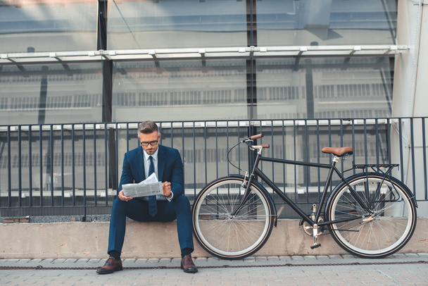 középső éves üzletember olvasó újság ülve, kerékpár Street közelében  - Fotó, kép