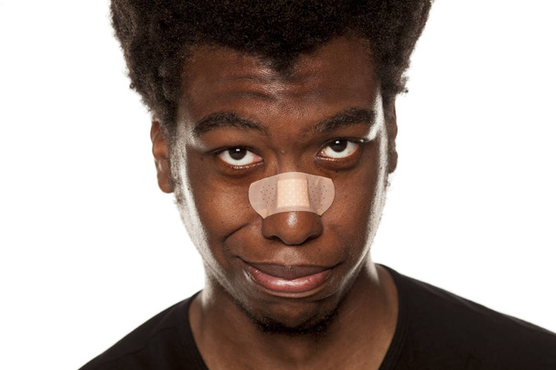 Πορτρέτο ενός νεαρού άνδρα αφρικανική αμερικανική με επίδεσμο ταινία πέρα από τη μύτη του σε λευκό φόντο - Φωτογραφία, εικόνα