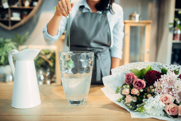 Vrouwelijke bloemist voegt meststof toe aan het water voor bloemen. Bloemschikken service, floristic business, floral winkel - Foto, afbeelding