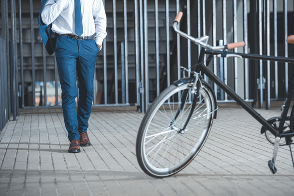 parked bicycle on street and low section of businessman walking behind - Photo, Image