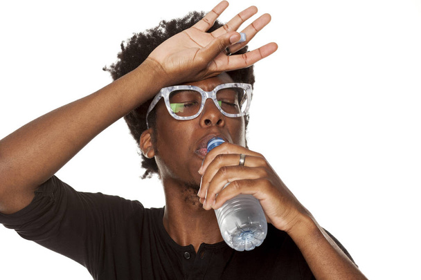 Retrato de un joven afroamericano bebiendo agua de una botella de plástico sobre un fondo blanco
 - Foto, Imagen