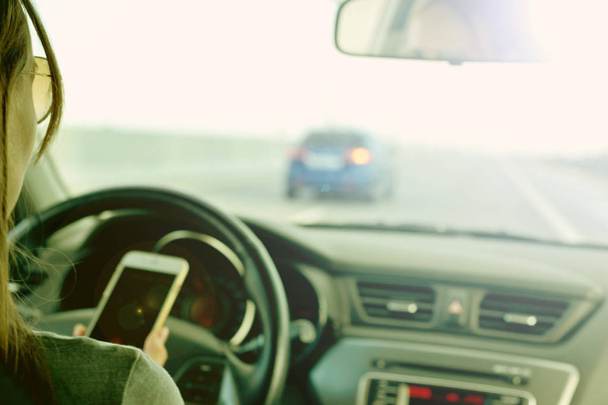 Fille tenant un smartphone sur la route, lors de la conduite d'une voiture. Derrière les commandes. Sécurité routière sur les routes en mains libres
 - Photo, image