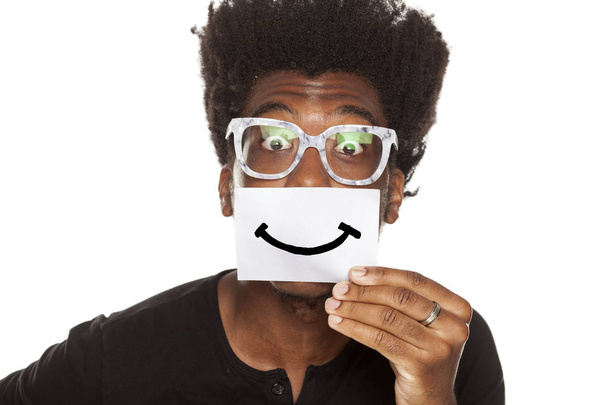 Jovem africano feliz segurando um sorriso desenhado em uma folha de papel em um fundo branco
 - Foto, Imagem