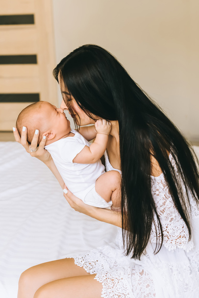 atraente jovem mãe e abraço com o bebê enquanto sentado na cama em casa
 - Foto, Imagem