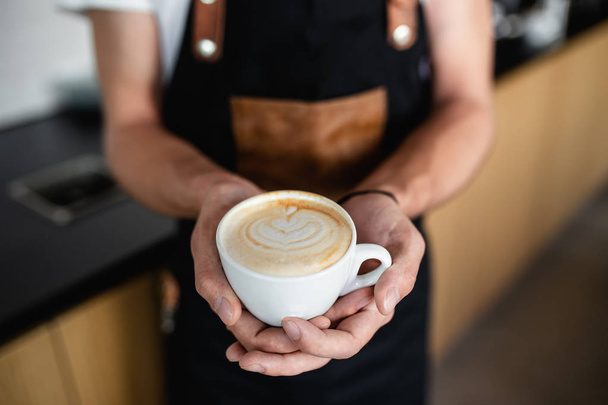 Professional barista holding cup of espresso coffee with milk. - Фото, изображение