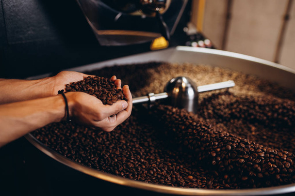 Freshly roasted coffee beans pouring from a large coffee roaster into the cooling cylinder. - Fotó, kép