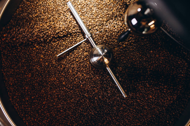 Freshly roasted coffee beans pouring from a large coffee roaster into the cooling cylinder. - Foto, Imagem