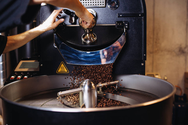 Φρεσκοτριμμένο φρυγμένους κόκκους καφέ που ξεχύνεται από roaster ένα μεγάλο καφέ στην ψύξη κύλινδρο. - Φωτογραφία, εικόνα
