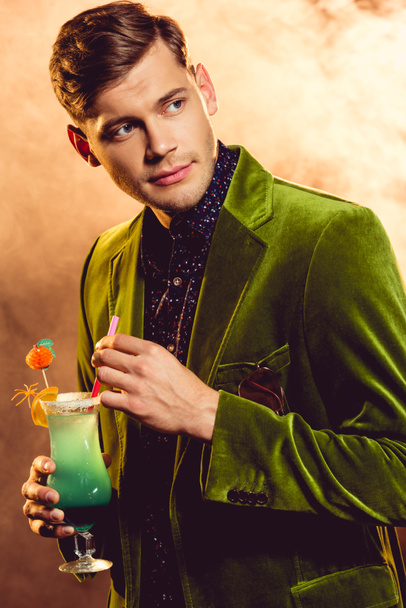 knappe man in groene jas vasthouden alcohol cocktail party met rook - Foto, afbeelding