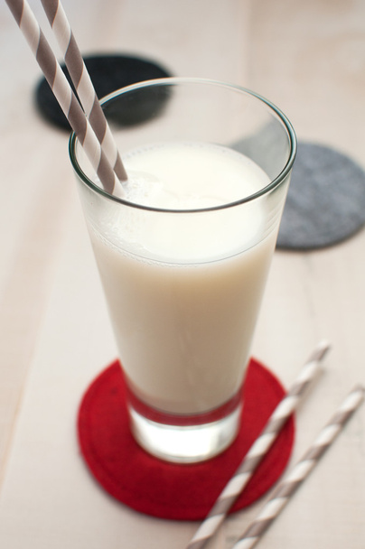 Glas Milch mit gestreiften Strohhalmen und Untersetzer - Foto, Bild