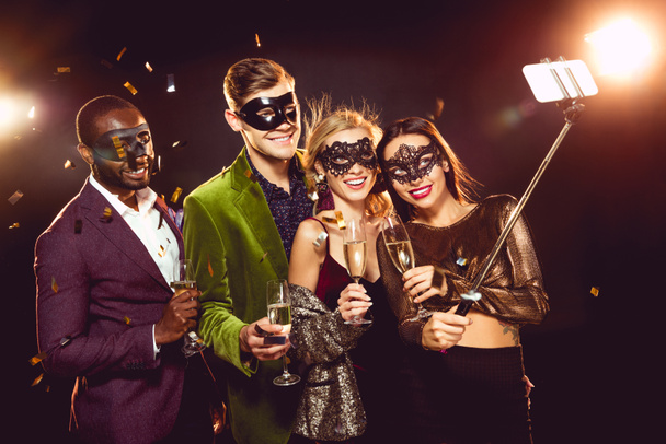 гламурні мультикультурні друзі в карнавальних масках беруть селфі на смартфон
 - Фото, зображення